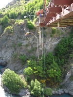 A young woman jumps from a bridge over a rocky gorge, with a rubber rope tied to her feet.
