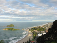 The ocean surrounds a couple of small islands to the left of a sandy beach.  On the right is a town.  Low sun casts shadows of the town across the beach.