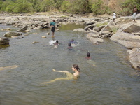 Jenny and a few small Nigeria boys paddling in a shallow pool surrounded by rocks.  Tress in the background.