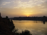 The sun sets behind an ancient city, reflected in a lake.