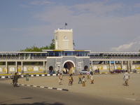 A painted cocrete wall with a gateway topped by a clock tower, outside is a sandy square.