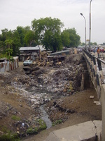 A road bridge over a small stream with both banks covered in rubbish.