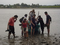 A boatload of people climb out into deep mud