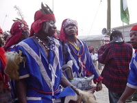 Two members of a masquerade group carrying an effigy, one looking directly into the camera