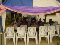 Group sitting in plastic chairs under an awning