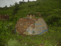 A lump of mortared rocks with 'IL EST MORT FEVRIER 1996' visible on the remaining concrete