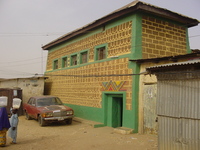 A green and yellow house with bright patterns painted above the door.  A Mercedes is parked outside.
