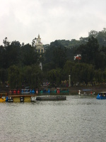 A lake with various small boats (some shaped like swans), with a building with a spire in the background.