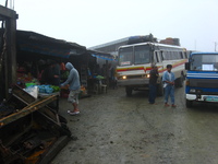 An old bus stopped outside some shacks on a muddy road.