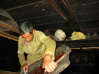 A man pours pounded rice from a wicker tray into a bucket lined with palm leaves.