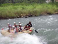 Six people and a guide in a rubber raft paddling through rapids.