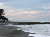 A surfer stands holding his fluorescent yellow board, at the end of a curving beach.