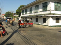 A street scene with horse-drawn carriages and motorbike-sidecar taxis.