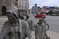 Metal statues of pedestrians walking towards a road, descending through the pavement and emerging on the other side.
