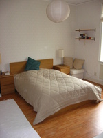 A wood-floored room with a double bed and a large round paper lampshade dangling from the ceiling.