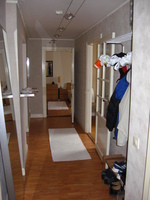 View down a wood-floored hallway, with doors on either side, through a door at the far end.