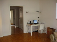 A wood-floored room with an open doorway.  Beside the doorway is a white desk with a laptop sitting on it (among other clutter).