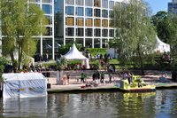 Between a hotel building and the river various tents and a stage have been built around a sand-covered area.