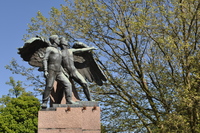 A greenish bronze statue of two standing figures on top of a pink granite column.