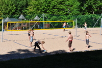Young people playing volleyball on a sand court in bright sunshine.