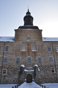 Looking across a frozen moat to the entrance of a castle.  Above the entrance archway the sun shines through windows.