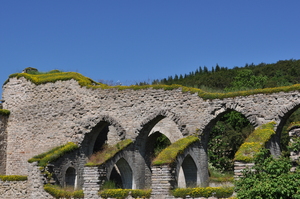 A ruined church, stone arches against a vivid blue sky.  A tree-covered hill in the backgroun.