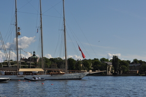 A white yacht surrounded by smaller vessels.  In the background is an island with trees and buildings.